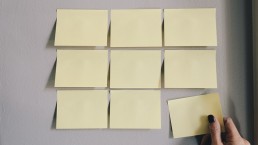 hand-removing-yellow-sticky-note-from-tiled-notes